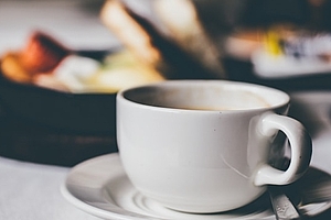 Eine Tasse Kaffee mit Essen im Hintergrund, serviert im Hotel Garni KEINATH in Stuttgart, wo Wohnen auf Zeit möglich ist.