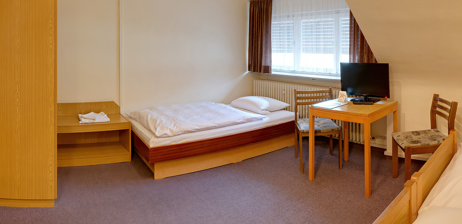 Blick auf ein großes Einzelbett unter dem Fenster neben einem Tisch mit zwei Stühlen