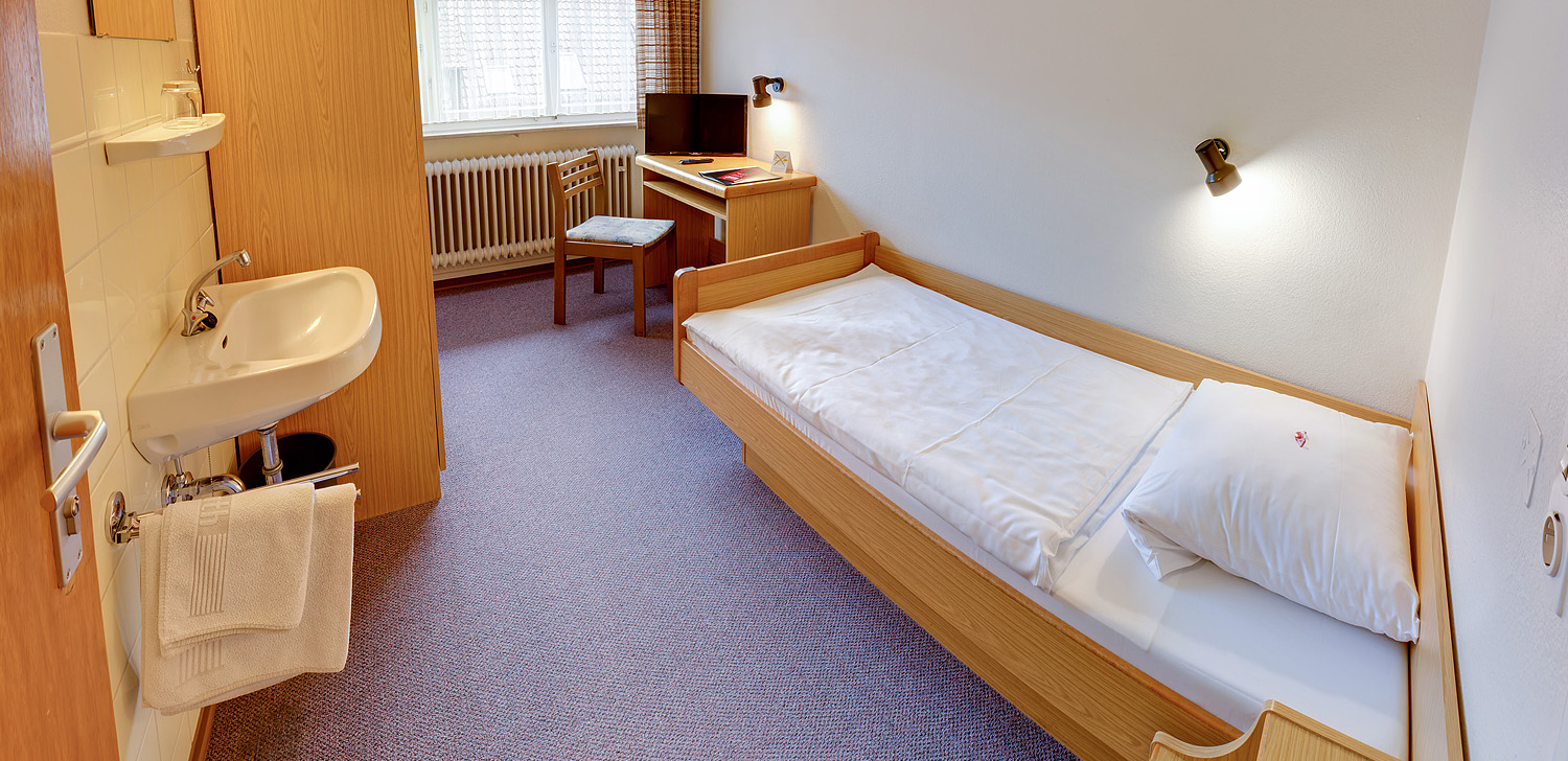 Einzelzimmer mit Waschbecken, Kleiderschrank und Tisch