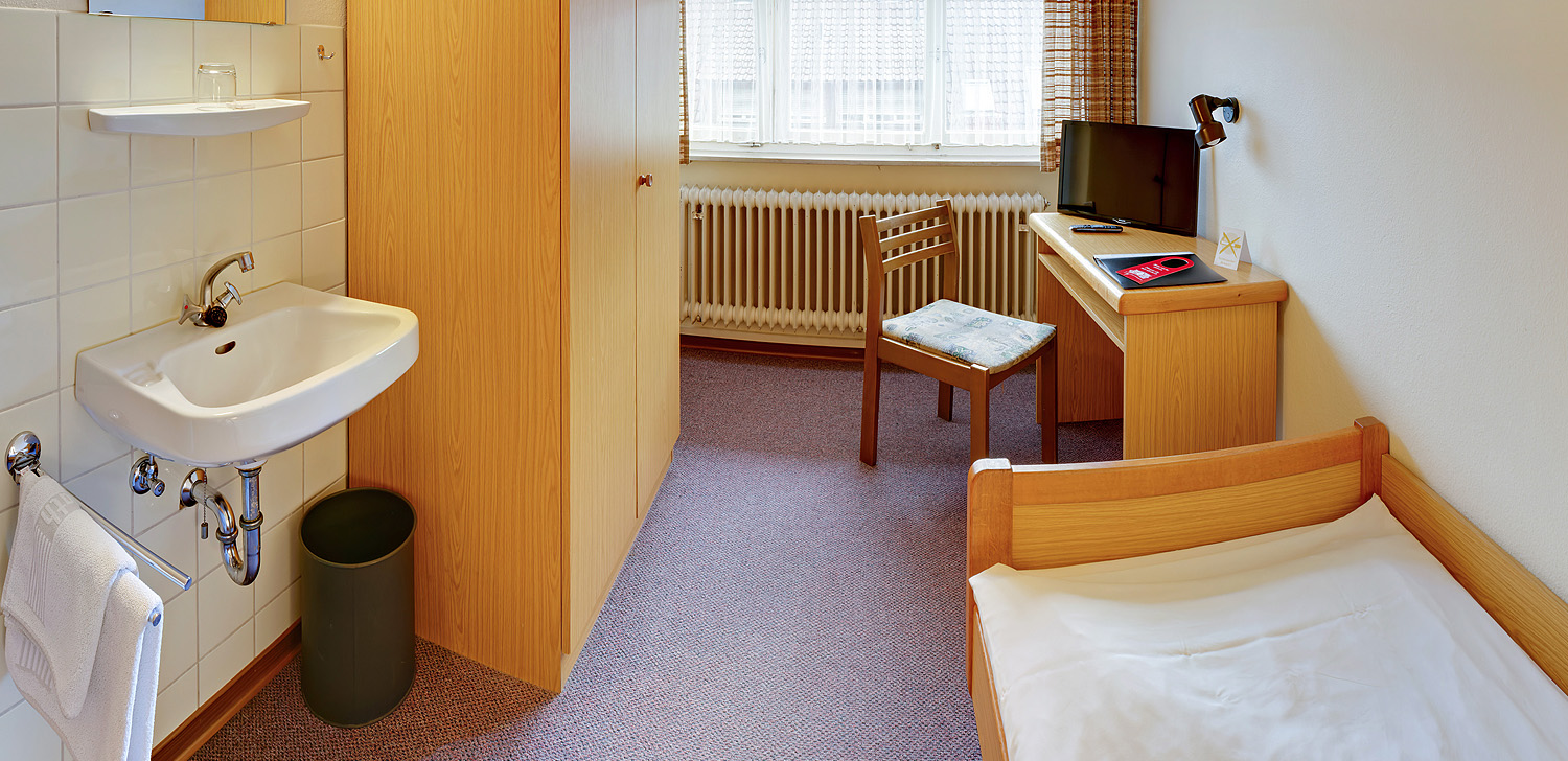 Blick aufs Einzelbett nebne einem Tisch mit Stuhl und Fernseher