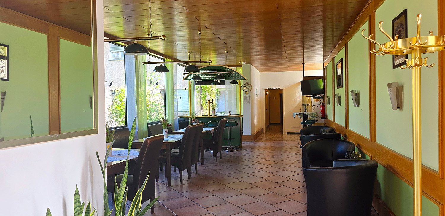 Heller Gastraum einer Unterkunft in Stuttgart mit drei Tischen mit grünen Decken, Stühlen und einer Bar im Hintergrund.