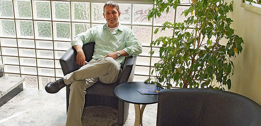 Ein Mann sitzt in einem blauen Loungesessel neben einer Pflanze und wartet auf sein Monteurzimmer in Stuttgart